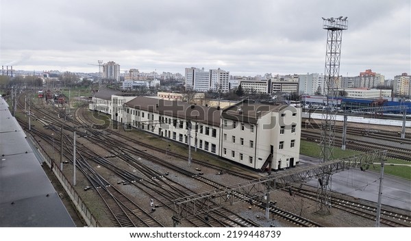 Many railroad tracks are laid on the territory of\
the railway station In the middle is a control building. The\
station has metal masts with lighting lanterns In the distance you\
can see the city block