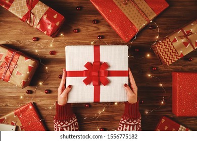 many red Christmas gifts with hands and garlands of lights on wooden background 