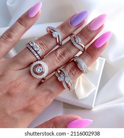 Many rings on a beautiful female hand on each finger on the background of a gift box on a white background top view. Six rings on a woman's hand. Silver and gold rings with diamonds