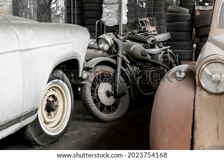 Many rusty abandoned forgotten antique oldtimer old car and motorcycles at junkyard factory storage warehouse indoors. Classic vintage retro vehicles detail garage workshop restore renovation station