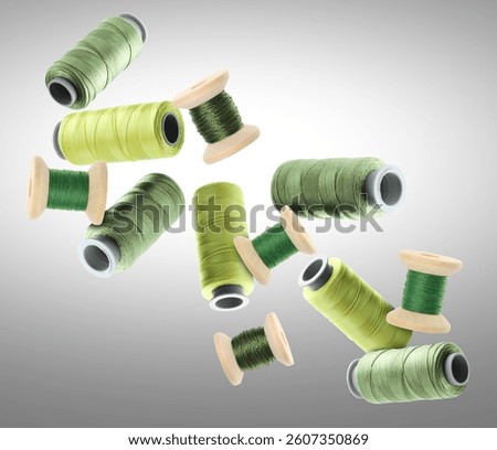 Many sewing threads in different shades of green flying on grey gradient background