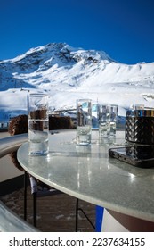 many shot glasses with liquor stand on table in front of snow covered mountains - Shutterstock ID 2237634155