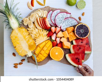 Many Sliced Colorful Tropical Fruit Plate On Serving Tray, Top View From Above. Summer Healthy Diet, Vegan Breakfast. Woman Hand Taking Watermelon Slice - POV.