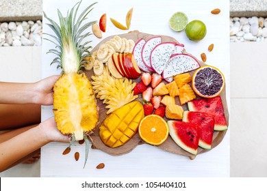 Many Sliced Colorful Tropical Fruit Plate On Serving Tray, Top View From Above. Summer Healthy Diet, Vegan Breakfast. Woman Hands Taking Pineapple Slice - POV.