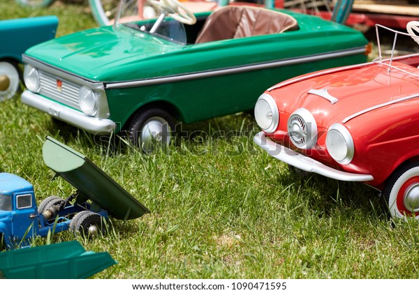 Many small antique toy cars for children on green\
grass in an outdoor park.