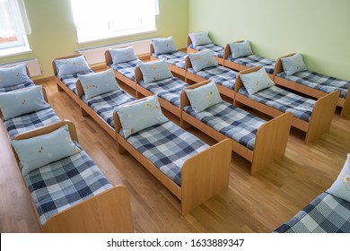 Many Small Beds With Fresh Linen In Daycare Preschool Empty Bedroom Interior For Comfortable Afternoon Nap Of The Kids.