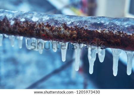 Many small icicles have frozen on a rusty pipe in the street in the winter