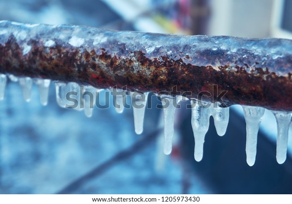 Many small icicles have frozen on a rusty pipe in\
the street in the winter