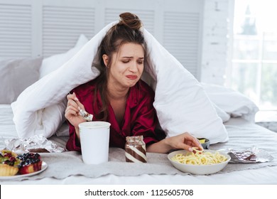 Many Snacks. Crying Nervous Woman Lying In Her Bed Surrounding By Snacks While Feeling Awful After Breakup