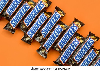 Many Snickers Chocolate Bars Lies On Pastel Orange Paper. Snickers Bars Are Produced By Mars Incorporated. Snickers Was Created By Franklin Clarence Mars In 1930