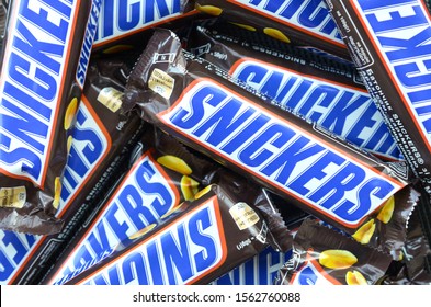 Many Snickers Chocolate Bars Stacked Close Up. Snickers Bars Are Produced By Mars Incorporated. Snickers Was Created By Franklin Clarence Mars In 1930