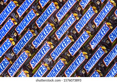 Many Snickers Chocolate Bars Stacked Close Up. Snickers Bars Are Produced By Mars Incorporated. Snickers Was Created By Franklin Clarence Mars In 1930