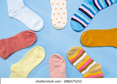 Many Socks Are Piled In A Circle In Blue Background. View From Above. Many Multicolored Socks Are Made In The Shape Of A Circle Or Sun. Space For Text. Clothes Made Of Knitwear.