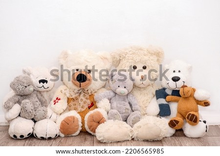 Many soft different bears are sitting on the background of a white wall
