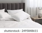 Many soft pillows on bed and bedside table at home