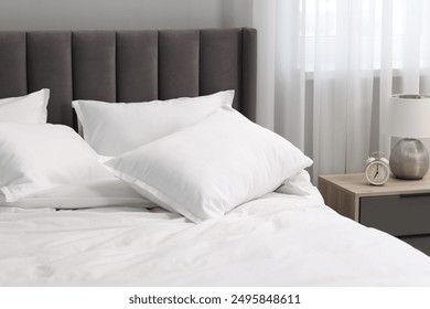 Many soft pillows on bed and bedside table at home