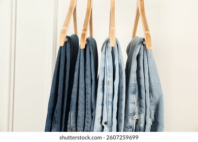 Many stylish jeans hanging against white wall