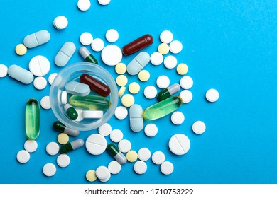 Many Tablets And Capsules Are Scattered And A Dosage Cup With Tablets. Close-up, Top View, On A Blue Background.