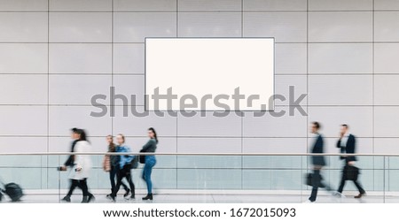 Many trade fair visitors walk under a blank billboard through a hall, copyspace for your individual text.
