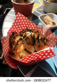 Many Wasps Feeding On A Muffin That Is Decorated With A Fondant Icing Bee, Table With Food In The Background.