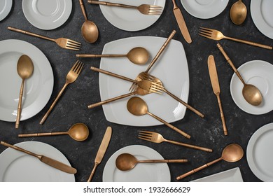 Many white empty ceramic plate and brass forks, knives and spoons on black background. Top view, close up