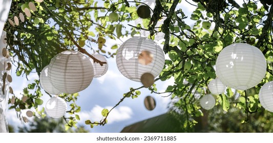 Many white lanterns, paper lanterns, glitter necklaces and white cloth decoratively hang festively in the apple tree. For festival, party, wedding - Powered by Shutterstock