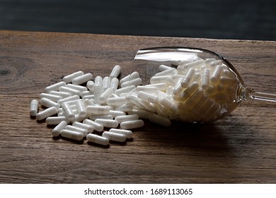 Many white medicine tablets spilled on wooden table. Pills spilled from wine glass lying on the table. Danger of alcohol and drugs, suicide.