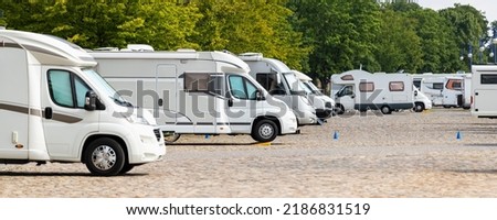 Many white modern campervan recreational motor home vehicles parked in row at camper park site Magdeburg city against Elbe river bridge. Motorhome campground stataion travel destination. RV lifestyle