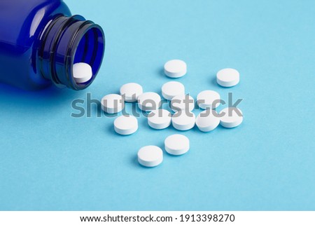 Many white tablets spilling out of package, Close up pills spilling out of pill bottle on blue background. Medicine, medical insurance or pharmacy concept close up with copy space.