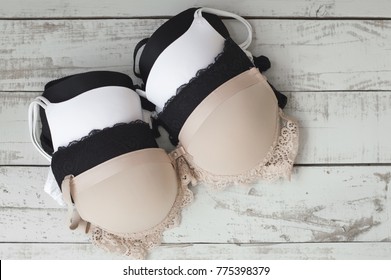 Many women's bra of beige, white and black colors on gray wooden background. Underwear fashion. Basic lingerie. Classic bra 