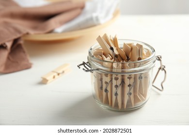 Many wooden clothespins in glass jar on white table, space for text
