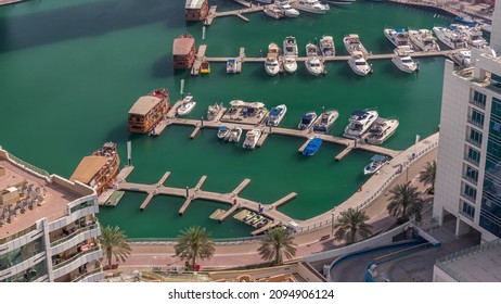 Many Yachts And Boats Are Parked In Harbor Aerial Timelapse. Dubai Marina Waterfront Walking Area. Modern Boat Is Riding The Creek.