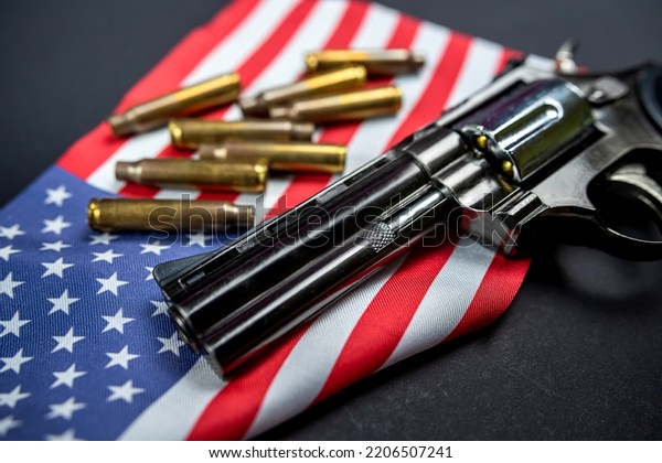 Many yellow bullets and a revolver gun on the
flag of the United States isolated on a black table. The concept of
arms trafficking on US territory or at a US shooting range.
Violence. Murders