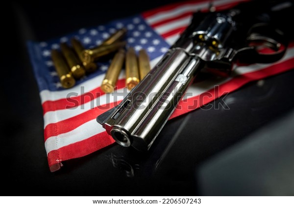 Many yellow bullets and a revolver gun on the\
flag of the United States isolated on a black table. The concept of\
arms trafficking on US territory or at a US shooting range.\
Violence. Murders