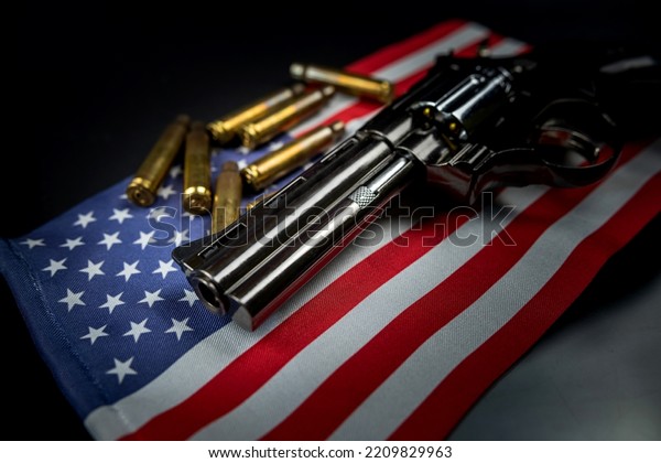 Many yellow bullets and a revolver gun on the\
flag of the United States isolated on a black table. The concept of\
arms trafficking on US territory or at a US shooting range.\
Violence. Murders