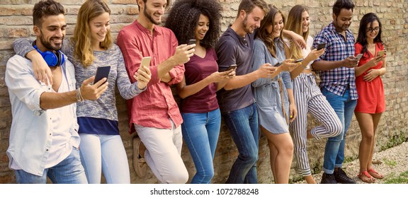 many young people using smart phones standing agaist a wall outside. concept of addiction to phone and gadgets wide header image