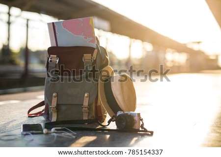 Map in Backpack ,Mobile phone with earphone and hat at the train station with a traveler.sun set, Travel concept.