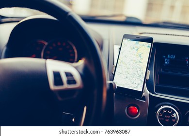 The map on the phone in the background of the dashboard. Black mobile phone with map gps navigation fixed in the mounting. Vintage style photo