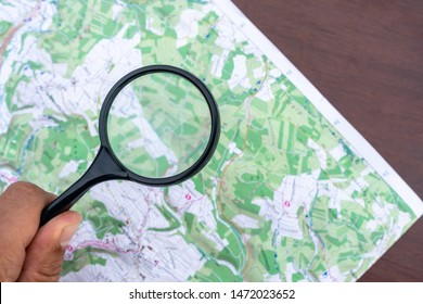 A map on a table. Detail topographic map. Man's hand holds a Magnifier, a Loupe. Terrain orientation. Trekking. Scouting Scout equipment for orientation in the forest. Orienteering Sports orientation