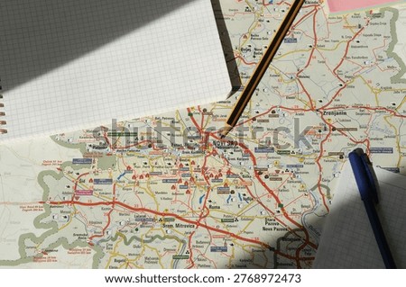Map themed workspace featuring notebook, pencil, and paper map for route planning and travel ideas. Highlights careful note taking, geography awareness, budgeting, goal setting, and scenic