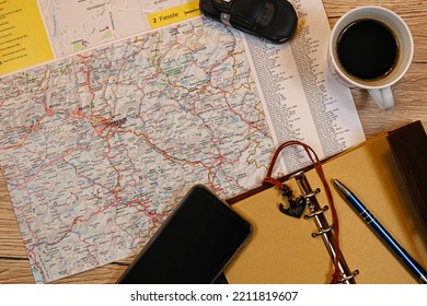 Map, Vintage Notepad, Pen, Mobile Phone, Car And A Cup Of Coffee Lying On A Wooden Desk