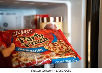 Maple Grove, Minnesota - April 15, 2020:  Hand Pulls Out A Totinos Party Pizza Frozen Pizza Out Of Freezer. Selective Focus On The Brand Name. Concept For Bored Eating During Quarantine