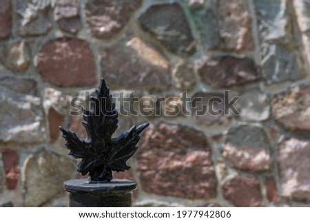 A maple leaf fence post top is seen against a backdrop of a stone wall on a bright sunny day in Bayfield, Ontario.