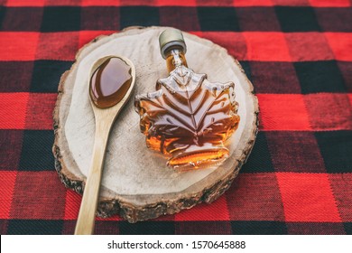 Maple syrup bottle Quebec cultural food traditional harvest top view on buffalo dining tablecloth background. Canada grade A amber sweet liquid in wooden spoon from sugar shack cabane a sucre farm.