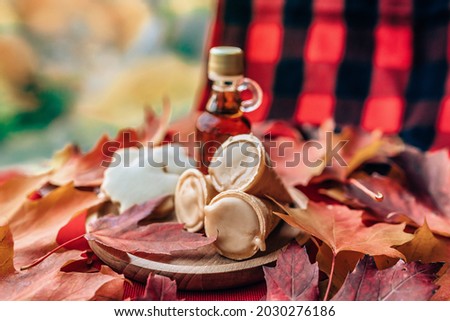 Maple syrup taffy cones dessert with traditional bottle and plaid cloth table - red leaves on table. Quebec local food.