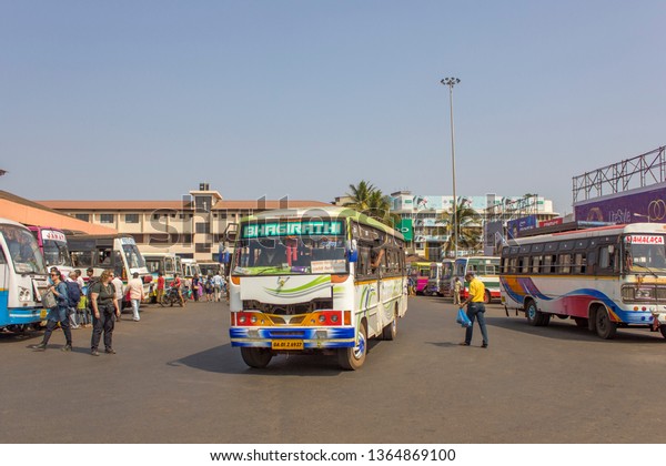 Mapusa, Goa/India - 24.01.2019: White\
Indian bus at the bus station against the backdrop of modern\
building, walking people and other bright colorful\
buses