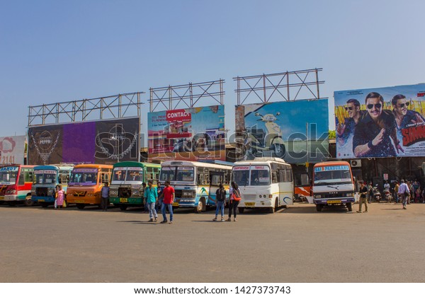 Mapusa,Goa/ India - 20.12.2018: Young Indian\
people are waiting near the parked bright colorful buses at the bus\
station under the\
billboards