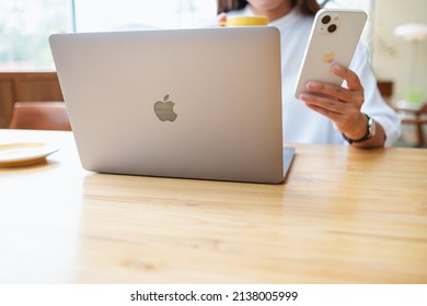 Mar 19th 2022 : A Woman Holding And Using Iphone 13 Smart Phone With Apple MacBook Pro Laptop Computer, Chiang Mai Thailand