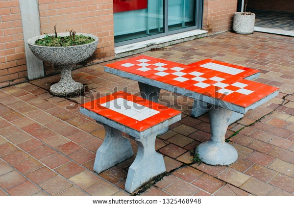Maranello, Italy\
- 03 26 2013: table and benches for playing chess in the yard. View\
of the streets of\
Maranello.