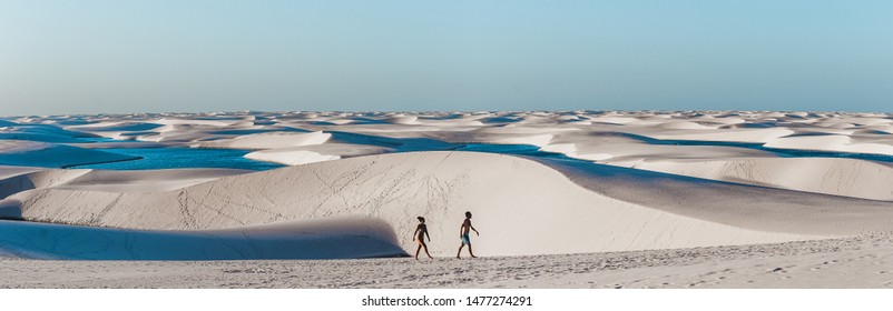 Lençóis Maranhenses, Brazil - July 24 2019: travel couple trek across giant sand dunes with lagoons in Lencois Maranhenses, one of the most breath-taking natural tourist attracts in North-East Brazil